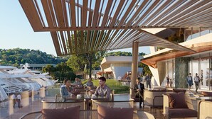 An outdoor seating area with tables and chairs, a wooden pergola overhead, and a view of a building and trees in the background. - VILLA HERMES/ Seaview / 7 min from the beach! (Vouliagmeni)