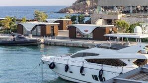 A marina with yachts docked, a modern building with 'Olear Bar Brown' signage, and a rocky coastline in the background. - VILLA HERMES/ Seaview / 7 min from the beach! (Vouliagmeni)