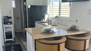 Een moderne keuken met een centraal eiland, twee barkrukken, een flatscreen televisie die boven het eiland is bevestigd, en een raam dat voor natuurlijk licht zorgt.