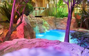 A pool area with a rocky landscape, a waterfall feature, and tropical vegetation.
