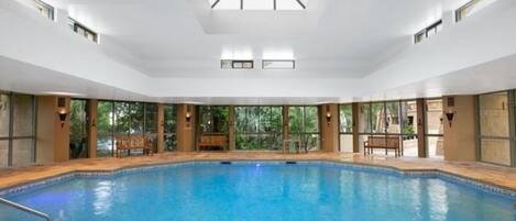 Una amplia piscina cubierta con paredes de vidrio transparente, bancos y techo de tragaluces.