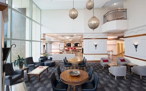 A spacious lobby with a central seating area, a staircase, and a view of a dining area.
