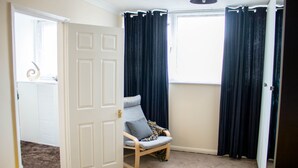 A room with a bed, a chair, a window with curtains, and a door.