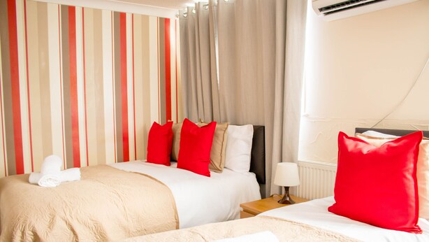A hotel room with two beds, striped curtains, a bedside table with a lamp, and a window with curtains.