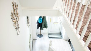 A staircase leading to a door with a doormat, a coat rack with clothes, and a wall-mounted plant.