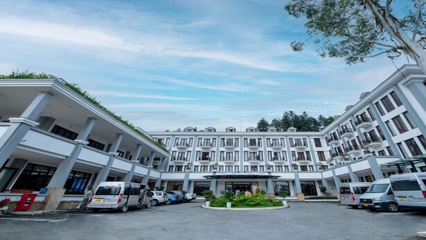 A multi-story hotel with a central courtyard, several balconies, and a variety of parked vehicles. - Convention Center Sapa Hotel (Sa Pa)