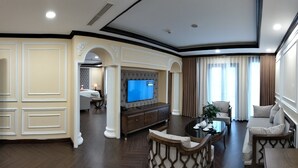 A spacious living room with a large flat-screen TV, a comfortable seating area, and a view of the adjacent bedroom. - Convention Center Sapa Hotel (Sa Pa)