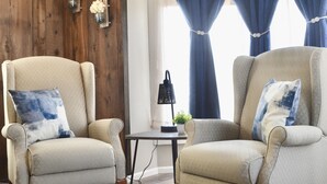 Une pièce comprenant deux fauteuils, une table basse ronde, un mur décoratif en bois et une fenêtre avec des rideaux bleus.
