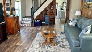 Un salon avec un escalier, un canapé bleu, une table basse en bois et une cuisine à l’arrière-plan.