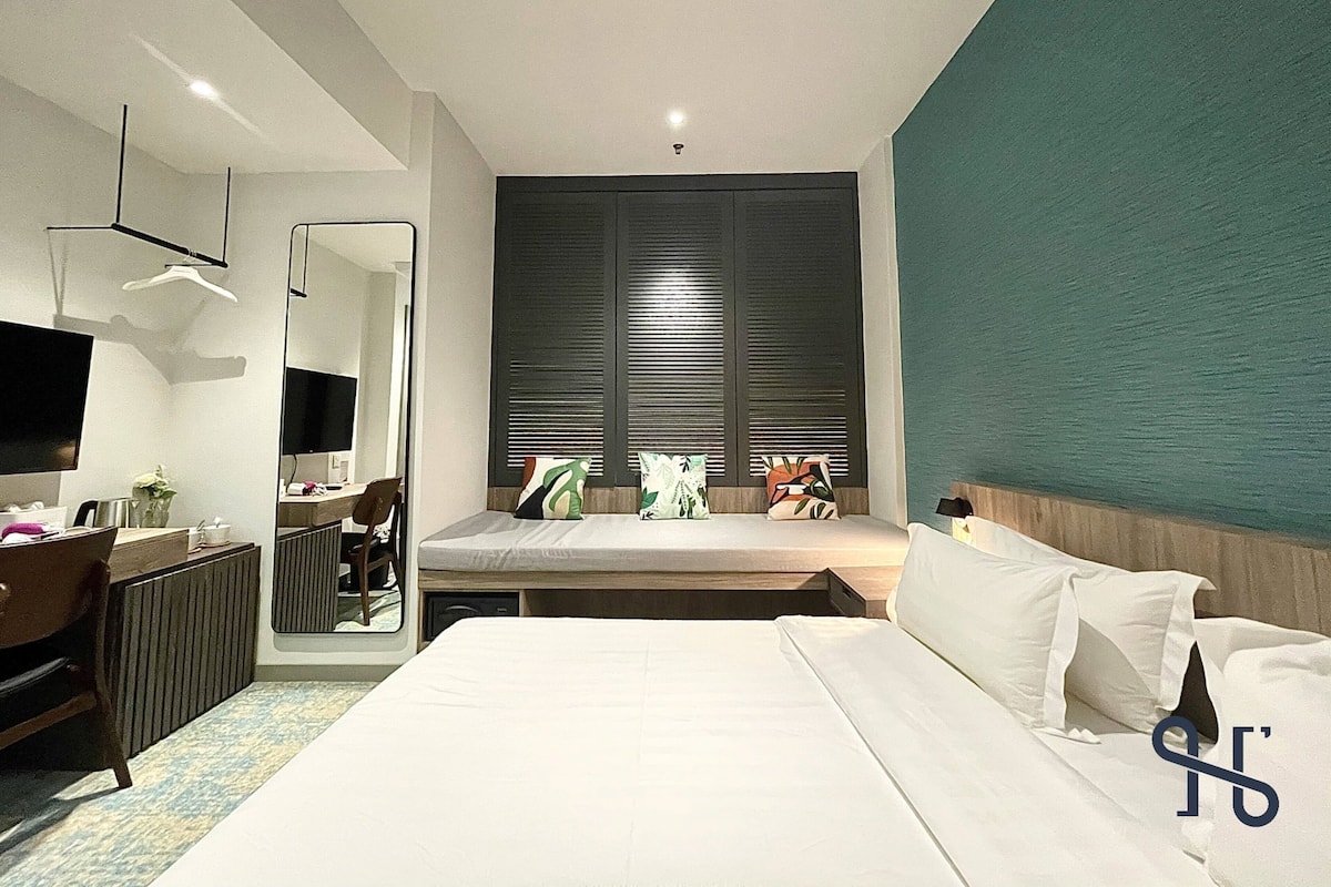 Een moderne hotelkamer met een groot bed, een bureau, een spiegel en een raam met zonwering.