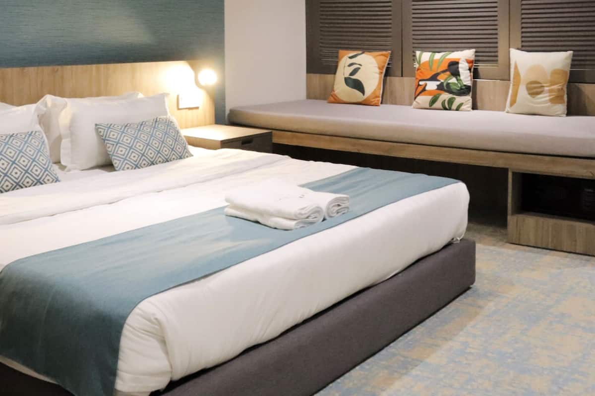 Een hotelkamer met een bed, nachtkastjes, een bankje en uitzicht.