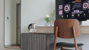 A modern room with a wooden chair, a radiator, a small table with a kettle, and a wall-mounted TV displaying an advertisement. - Homi Breeze 和逸微风 (Kota Kinabalu)