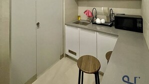 A compact kitchen with white cabinets, a microwave, a sink, and a small stool. - Homi Breeze 和逸微风 (Kota Kinabalu)