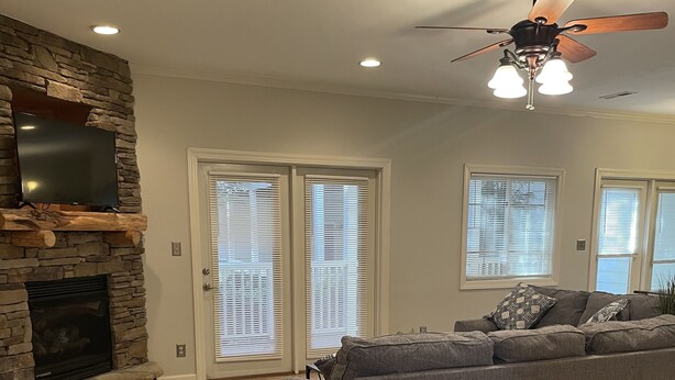 A spacious living room with a stone fireplace, a large gray sectional sofa, and a ceiling fan. - Elegant Mountain Townhome in Banner Elk (Banner Elk)