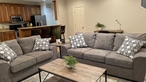 A living room with two grey sofas, a wooden coffee table, and a kitchen in the background. - Elegant Mountain Townhome in Banner Elk (Banner Elk)