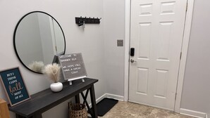 A clean, modern entryway with a white door, a round mirror, a welcome sign, a framed quote, and a small table with decorative items. - Elegant Mountain Townhome in Banner Elk (Banner Elk)