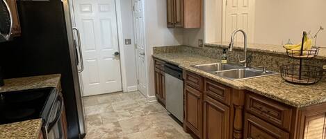 Una cocina con encimeras de granito, armarios de madera, un lavamanos de acero inoxidable y un refrigerador negro.
