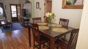 Een eetgedeelte met een houten tafel, vier stoelen en een vaas met bloemen.