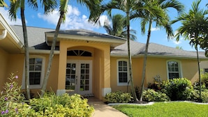 A residential house with a yellow facade, a covered front porch, and palm trees. - ---BEAUTIFUL TROPICAL GARDEN HEATED POOL HOME ---
/AN OPTION BOAT RENTAL (Cape Coral)