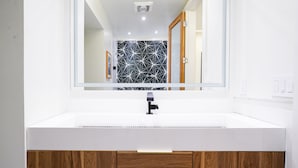 Une salle de bain avec un lavabo blanc, un miroir et un mur orné d’un motif géométrique.