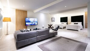 Une chambre d’hôtel moderne avec un canapé gris, un grand téléviseur à écran plat, un lit avec une tête de lit noire et un mur d’accent en bois.