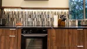 Une cuisine moderne avec des finitions en bois, un four encastré et un pare-feu orné d’un motif à rayures.