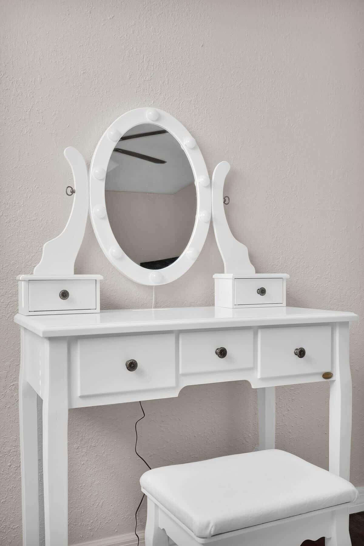 Une coiffeuse blanche avec un miroir, deux tiroirs et un banc.