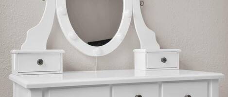 Une coiffeuse blanche avec un miroir, deux tiroirs et un banc.