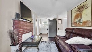 A living room with a fireplace, a sofa, a coffee table, and a TV mounted on the wall. - Smart Saver Townhouse, Family Friendly, Close to NAS Jax, Long-Term, Washer and Dryer (Jacksonville)