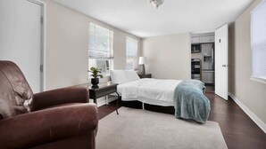 A bedroom with a bed, bedside table, lamp, and a view of the kitchen. - Smart Saver Townhouse, Family Friendly, Close to NAS Jax, Long-Term, Washer and Dryer (Jacksonville)