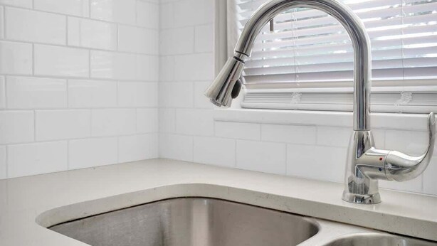 A kitchen with a stainless steel sink, white tiled backsplash, and a window with blinds. - Smart Saver Townhouse, Family Friendly, Close to NAS Jax, Long-Term, Washer and Dryer (Jacksonville)