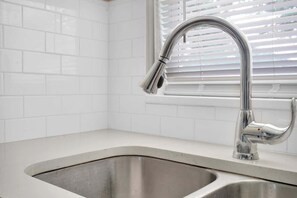 A kitchen with a stainless steel sink, white tiled backsplash, and a window with blinds. - Smart Saver Townhouse, Family Friendly, Close to NAS Jax, Long-Term, Washer and Dryer (Jacksonville)