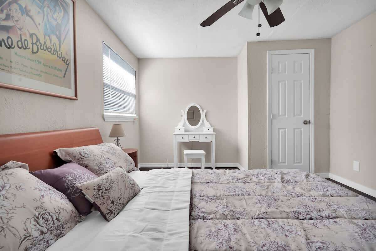 Un dormitorio con cama, cómoda, espejo, puerta y ventilador de techo.