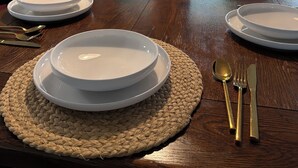 A dining table set with white plates, gold cutlery, and a white vase with yellow flowers.