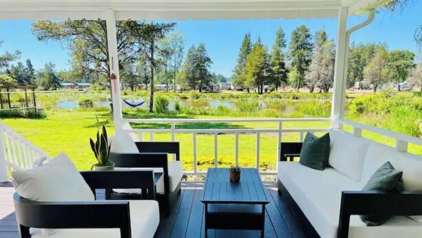 A covered outdoor seating area with a view of a pond and trees.
