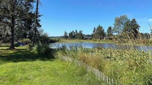 A grassy area with a hammock, a wooden fence, and a body of water.