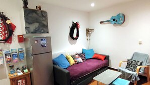 Un espace de vie compact comprenant un canapé, une petite table, un réfrigérateur et une guitare accrochée au mur.