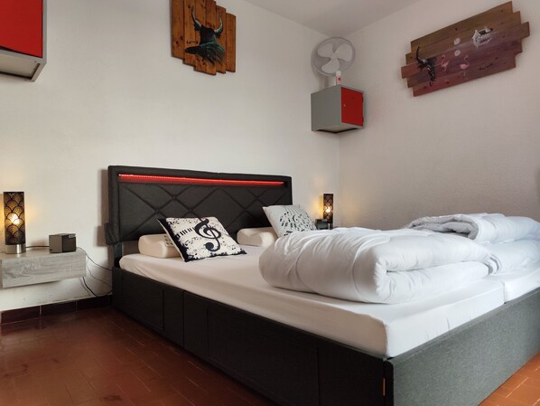 Une chambre moderne comprenant un lit, des tables de chevet, un ventilateur fixé au mur et un panneau décoratif en bois.