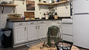 Une cuisine moderne avec des meubles blancs, des étagères en bois et une table de salle à manger ronde surmontée d’un panier noir.