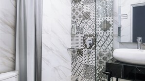 Un baño con inodoro blanco, ducha con puerta de vidrio, lavamanos con encimera negra y azulejos decorativos en las paredes.