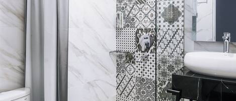 A bathroom with a white toilet, a shower with a glass door, a sink with a black countertop, and patterned tiles on the walls.