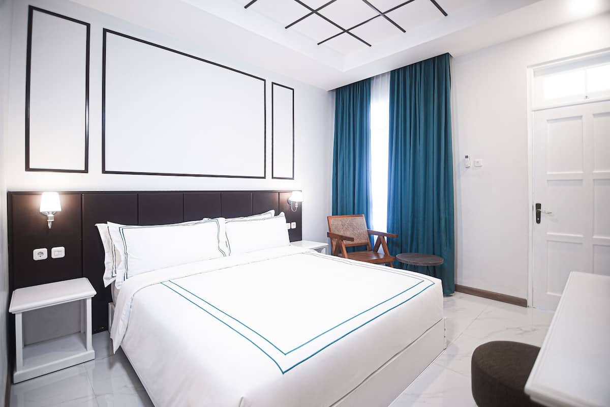 A hotel room with a large bed, bedside tables, a chair, and a small table.