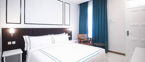 A hotel room with a large bed, bedside tables, a chair, and a small table.