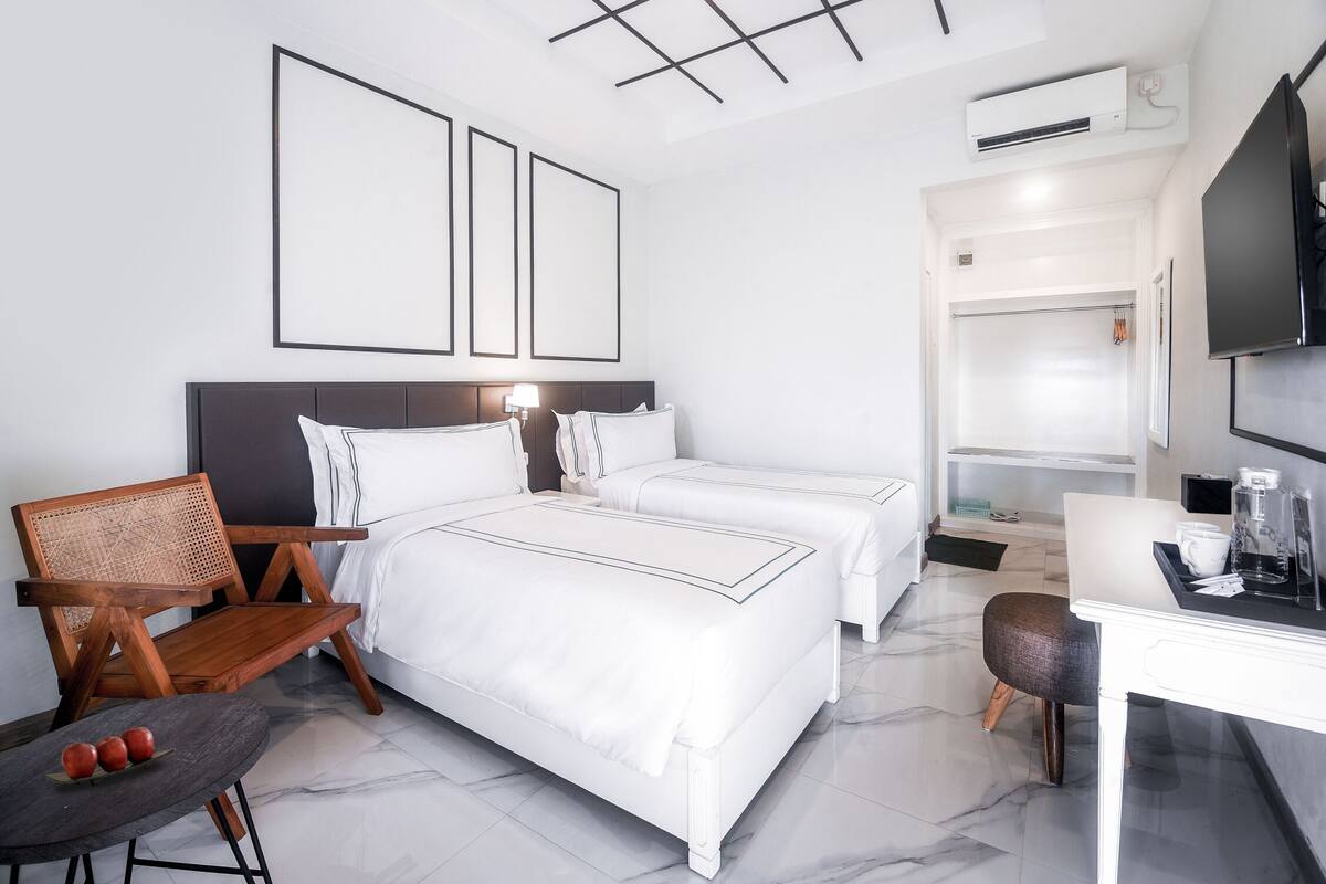 A modern hotel room with two beds, a desk, a chair, and a television.