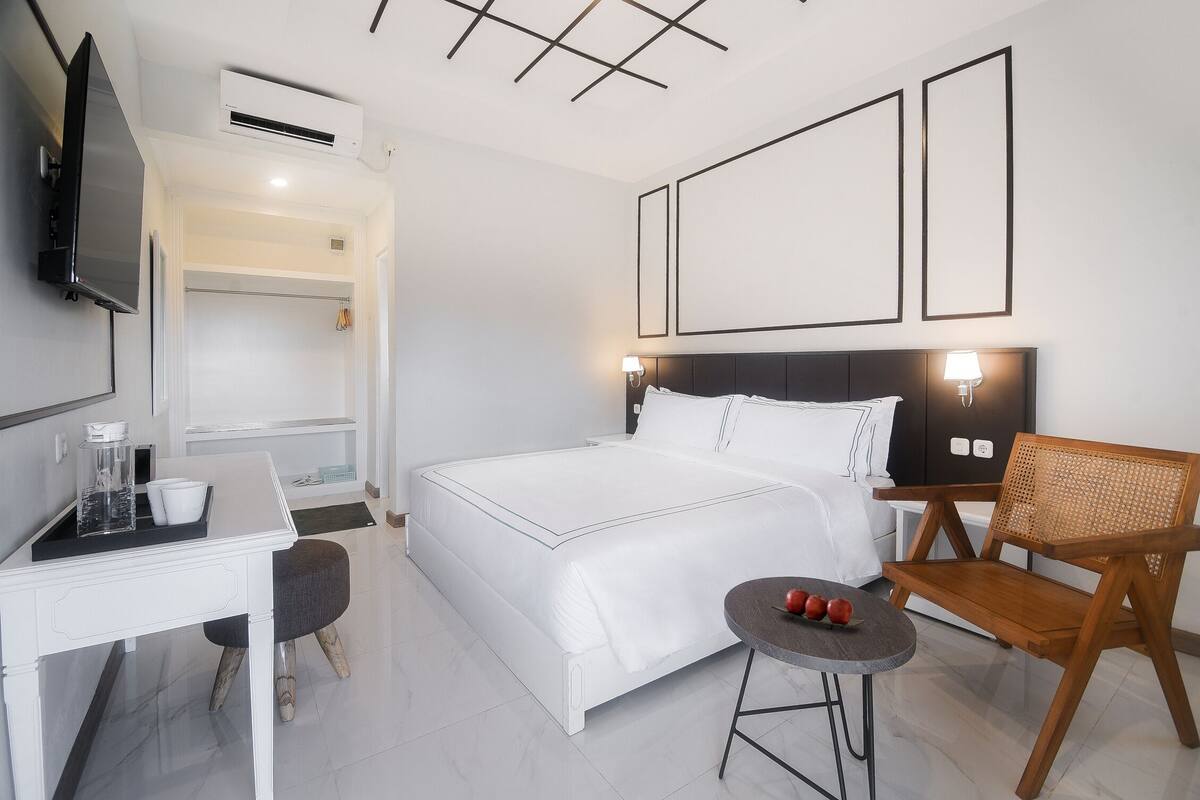 A modern hotel room with a bed, a desk, a chair, and a TV.