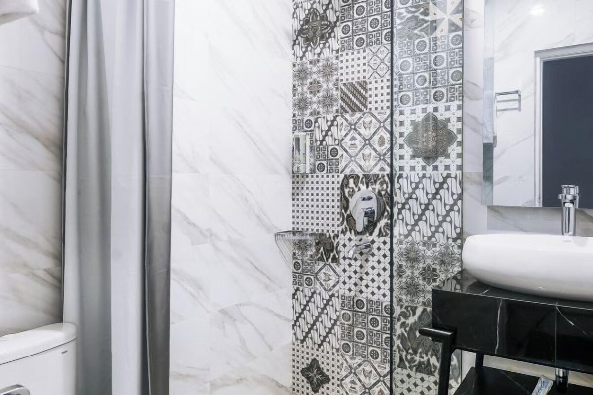 A bathroom with a patterned tile wall, a white sink, and a glass shower enclosure.