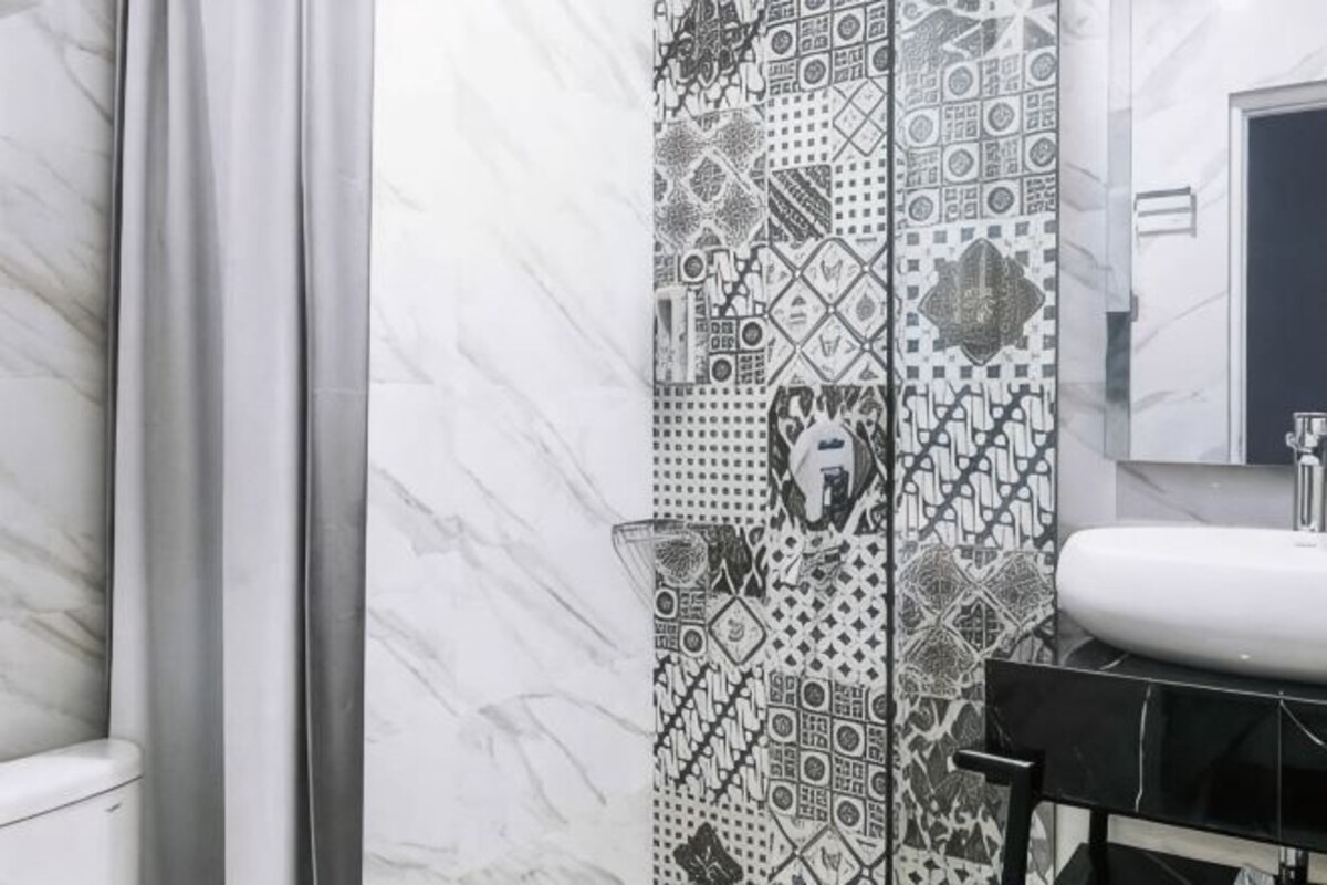 A bathroom with a patterned tile wall, a white sink, and a mirror.