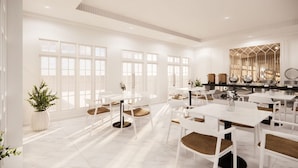 A spacious dining area with white tables and chairs, large windows, and a modern chandelier.