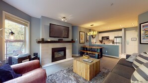 Uma sala de estar moderna com lareira, televisão montada acima e uma área de jantar com mesa e cadeiras de madeira.