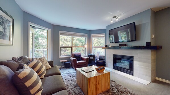 A modern living room with a fireplace, a sofa, a coffee table, and a television mounted on the wall.